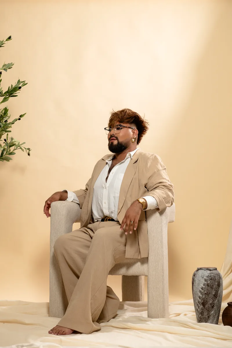 JoeJoe, owner and master stylist, seated in a cream armchair in a linen suit and gold watch