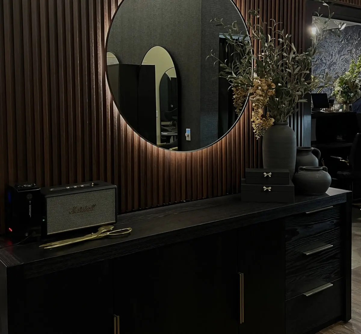 Backlit round mirror on a wood slat wall above a black console