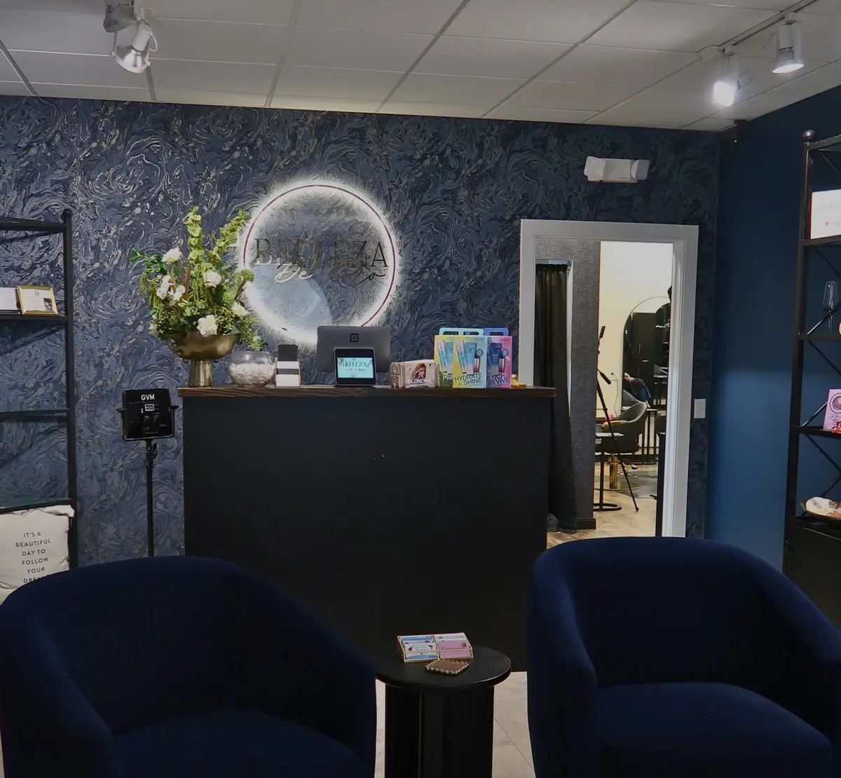 Reception desk with a lit round mirror and two navy velvet lounge chairs