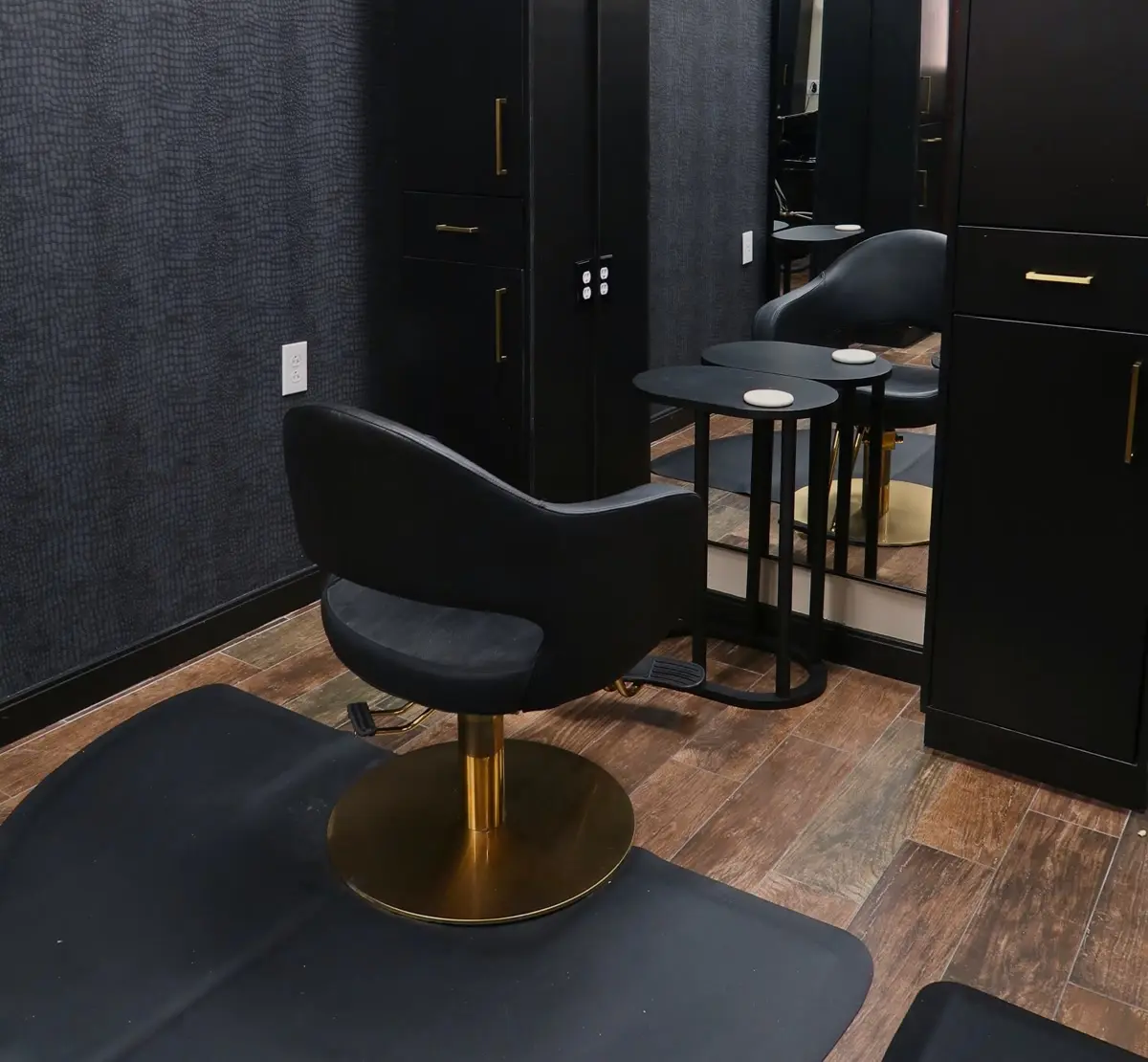 A private styling station with a black chair on a gold base, arched mirror and side table